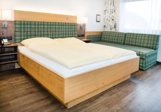 Schlafbereich im Komfortzimmer Deluxe Abendsonne im Landhotel Tirolerhof in Oberau in der Wildschönau mit Doppelbett und Couch