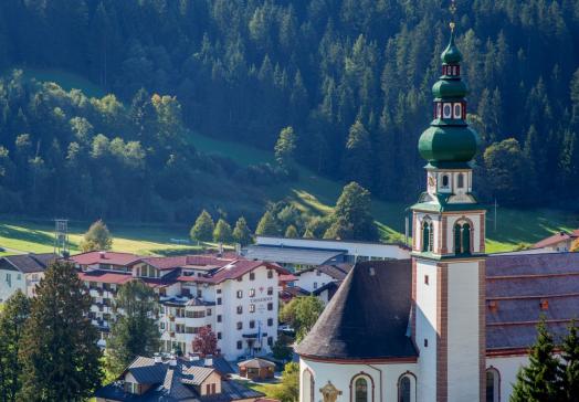 Landhotel Tirolerhof in Oberau in der Wildschönau mit Dorfkirche und Berglandschaft im Sommer