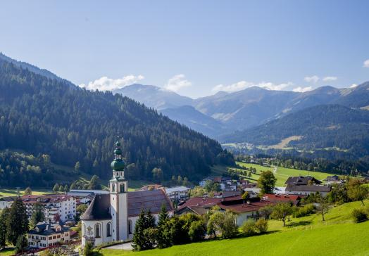 Sommerlicher Panoramablick auf Oberau in der Wildschönau mit Dorfkirche, Berglandschaft und dem Landhotel Tirolerhof.