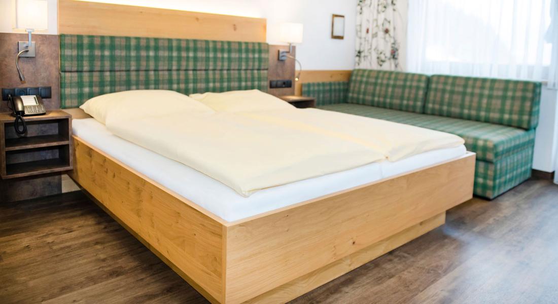 Schlafbereich im Komfortzimmer Deluxe Abendsonne im Landhotel Tirolerhof in Oberau in der Wildschönau mit Doppelbett und Couch