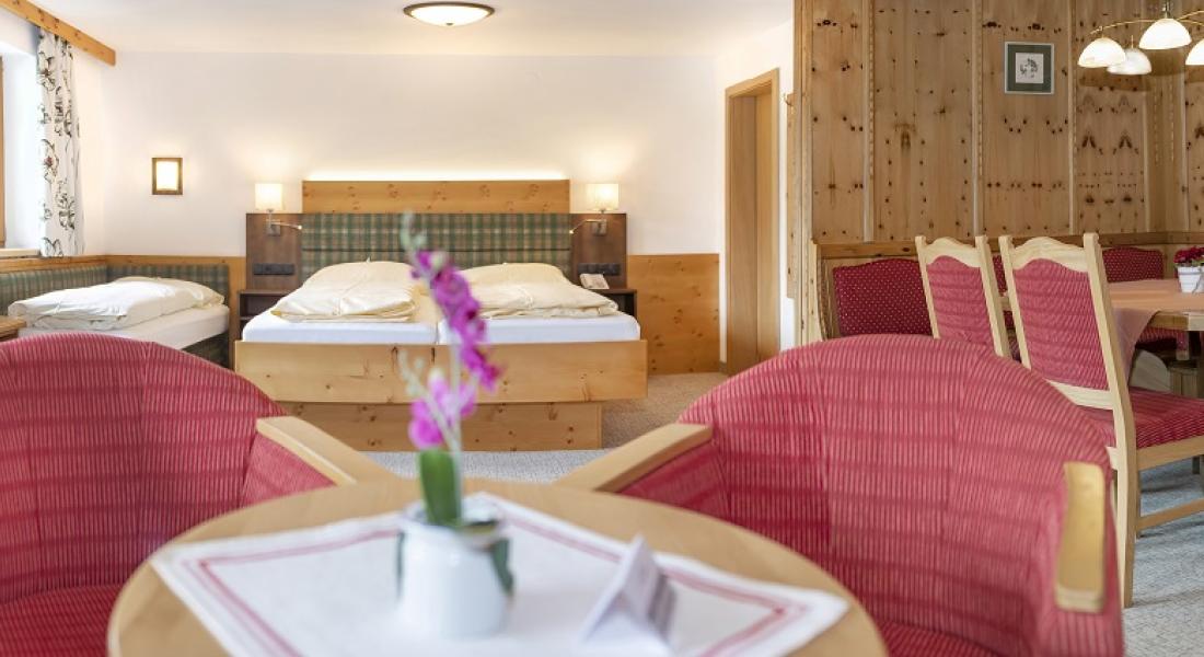 Living and sleeping area of ​​the pine-paneled room in the Landhotel Tirolerhof in Oberau in the Wildschönau region, featuring pine wood furnishings and a seating area.